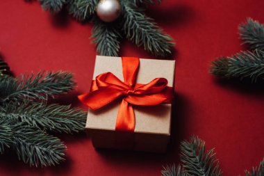 Noel konsepti. Kırmızı toplu Noel hediyesi kutusu ve kırmızı arka planda çam kozalaklı dallar