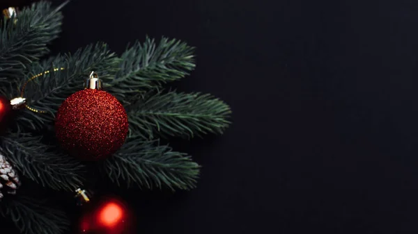 Ramo dell'albero di Natale con palline di Natale rosse su sfondo nero. Biglietto di auguri natalizio con spazio. Posa piatta, vista dall'alto — Foto Stock