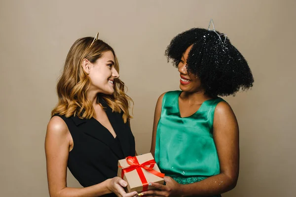 Una joven mujer negra le está dando a su novia caucásica un regalo de vacaciones. Concepto de Año Nuevo, Cumpleaños o Cumpleaños — Foto de Stock