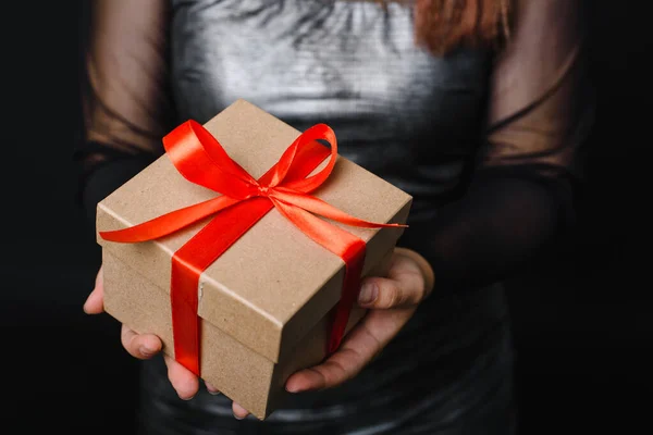 Uma jovem está segurando um presente de Natal com uma fita vermelha em suas mãos. Conceito de presente para o ano novo. Espaço de cópia — Fotografia de Stock