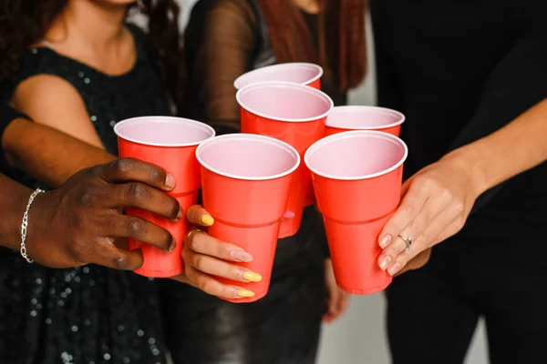 Waist up of six friends having fun and drinking alcohol during New Year party, isolated on white background. A group of cheerful friends of different nationalities clink glasses with red glasses at a