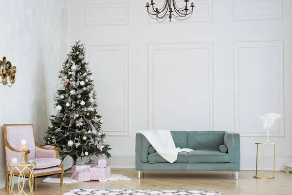 Lehký vánoční interiér. Vánoční stromek s dárky pod ním v béžové a růžové tóny vedle modré pohovky — Stock fotografie