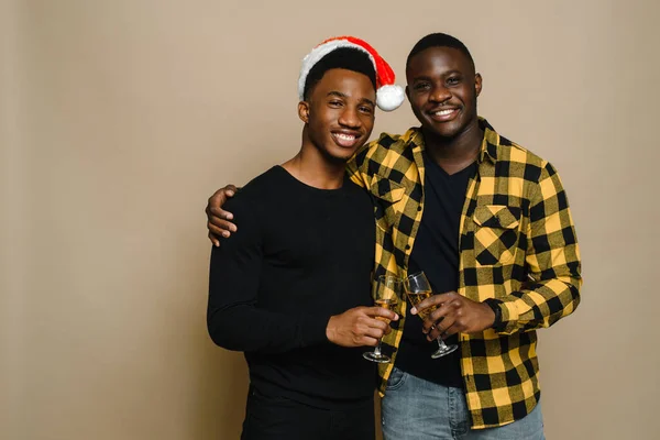 Boldog családi portré karácsonykor, meleg férfi pár bézs háttérrel. Egy pár fekete férfi szerelmes pohárban pezsgővel. Egészségedre. Ünnepeljük a karácsonyt és az új évet — Stock Fotó