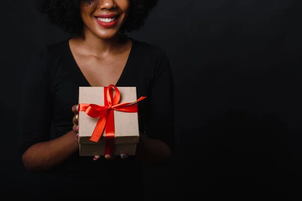 Happy black young woman with afro is holding a holiday gift in her hands and smiling. Gift giving and Christmas shopping concept. Black Friday