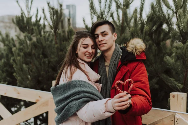 A young couple are holding a heart shaped candy cane and hugging. City portrait of lovers. Christmas, new year and love concept. Outdoor — Stock Photo, Image