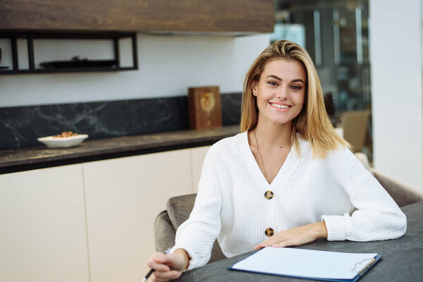 Молодая женщина работает на кухне и что-то пишет в блокноте. Деловая женщина работает удаленно из дома