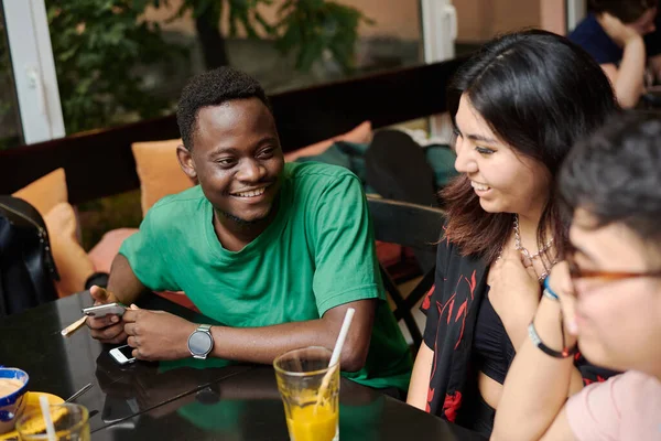 Egy fiatal fekete férfi viccet mesél a barátnőjének, körülvéve barátokkal egy modern kávézóban. — Stock Fotó