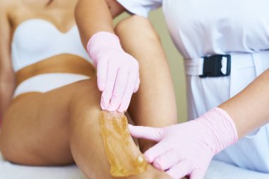 Genç ve güzel bir güzellik uzmanı müşterinin bacağına şeker yapıştırıcısı sürüyor. Titreyerek saç kesme işlemi. Güzellik uzmanı genç kadını tüy döküyor.