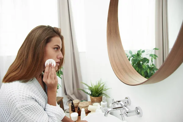 Mujer con una esponja de algodón problema de la piel. Una foto de una chica feliz limpiándose la cara con almohadillas de algodón sobre el baño. Hermosa cara de mujer joven con piel limpia y fresca — Foto de Stock