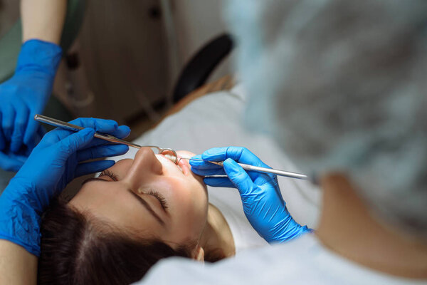 Medical treatment at the dentist office. Female dentist and assistant in dental office examining young woman with tools in dental clinic
