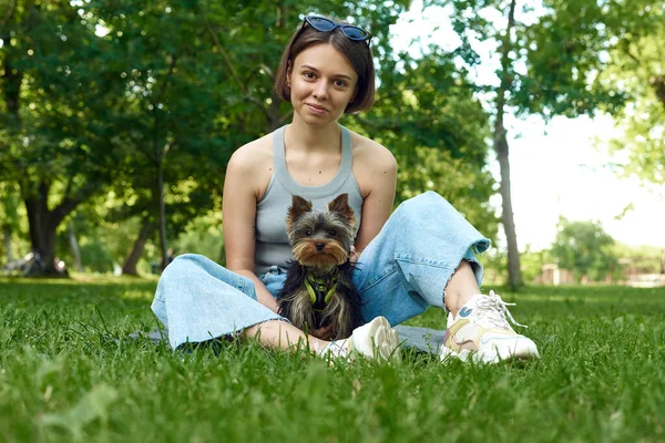 Милая красивая женщина с маленьким йоркширским терьером в парке на открытом воздухе. Портрет в стиле жизни — стоковое фото