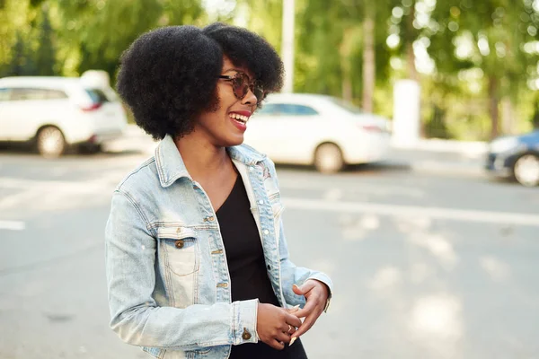 Egy afro-amerikai nő áll a város utcáján napszemüvegben és nevet. — Stock Fotó