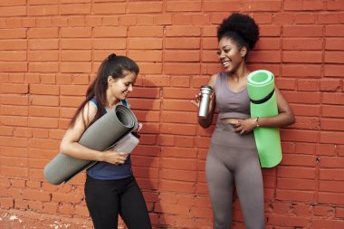 Spor üniformalı iki gülen kız arkadaş, tuğla duvarın arka planında iletişim kuruyor.