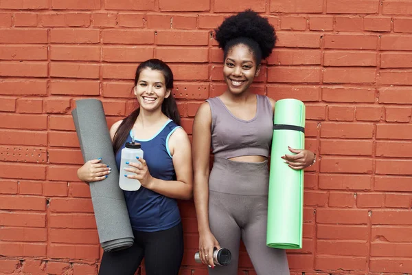 Spor üniformalı iki gülen kız arkadaş, tuğla duvarın arka planında iletişim kuruyor.