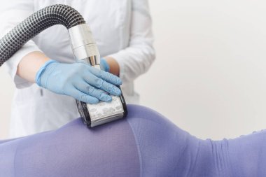 Güzellik uzmanı mor takım elbiseli genç bir kadının poposuna LPG masajı yapıyor. Lenfatik drenaj masajı. Zayıflatıcı tedaviler