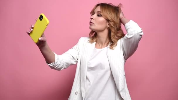 Cute young woman takes a selfie in the studio on a pink background — Stock Video