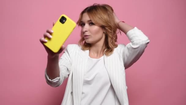 Mujer divertida de moda posando tomando selfie uso de teléfono inteligente aislado en fondo de estudio rosa. Concepto de vida — Vídeo de stock