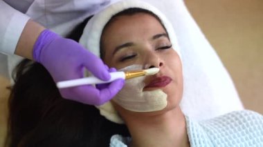 Mükemmel bir güzellik uzmanı, yaşlanma önleyici beyaz bir maskeyi yüzüne bir fırçayla sürer.