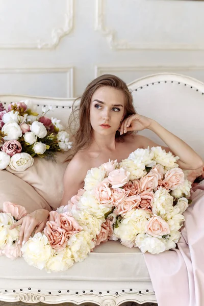 Beauty, fashion. Wedding style. Portrait of a beautiful bride young woman in an elegant pink dress of roses, peonies and flowers, sitting on a sofa in the interior — Foto de Stock