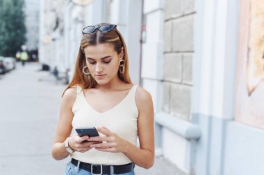 Mutlu, başarılı, gülümseyen bir kadın, açık sokak arka planında online alışveriş yapmak için akıllı telefonu kullanıyor. Kapat.