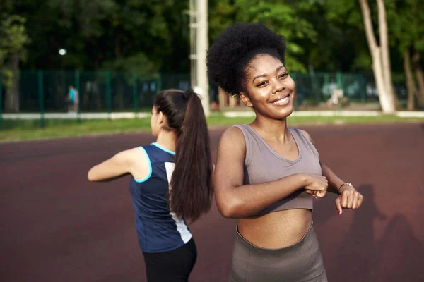 Två passar leende ung kvinna arbetar tillsammans i en park gör stretching motion och handförlängningar för att förbättra smidighet — Stockfoto