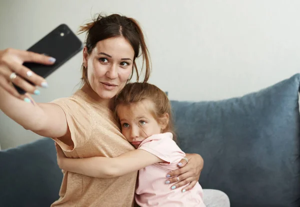 Genç beyaz anne ve küçük tatlı kızı telefonda selfie çekiyorlar, dillerini gösteriyorlar. Evde birlikte eğlenmek için. — Stok fotoğraf