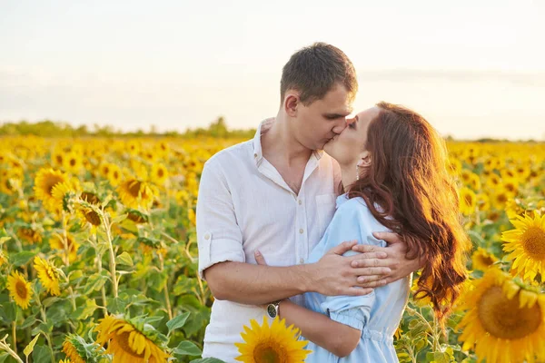 Lächelndes glückliches Paar, das sich inmitten eines Feldes mit Sonnenblumen umarmt. Sonnenblendung. Romantisches Paar im Liebesmoment — Stockfoto