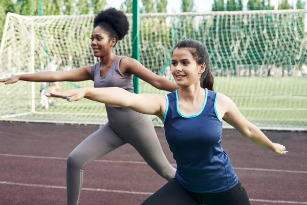 Två passform leende ung kvinna arbetar tillsammans i en park gör stretching motion och ben förlängningar för att förbättra smidighet — Stockfoto
