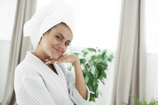 Mulher bonita em roupão de banho e toalha na cabeça sorrindo para a câmera no banheiro — Fotografia de Stock