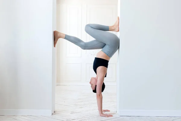 En ung kvinna utövar yoga och står på armarna i ett ljust rum. Ung attraktiv yogi kvinna praktiserar yoga koncept — Stockfoto