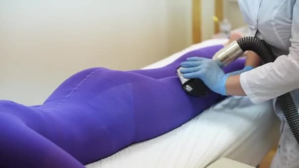 Žena ve speciálním purpurovém obleku na masáž proti celulitidě v lázeňském salonu. Masážní procedura. Ruce terapeuta držícího lipomasážní nástroj — Stock video