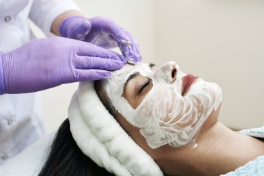Spa konsepti. Güzellik salonunda besin maskesi takan genç bir kadın, yakın plan. Güzellik uzmanı müşterilerin yüzüne nemlendirici bir maske takar.