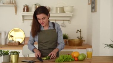 Güzel bir kadın, ahşap bir mutfakta sebze hazırlıyor ve akıllı telefondan yemek tarifine bakıyor. Genç bir kadın yemek kursu için web sitesine bakıyor ve gülümsüyor