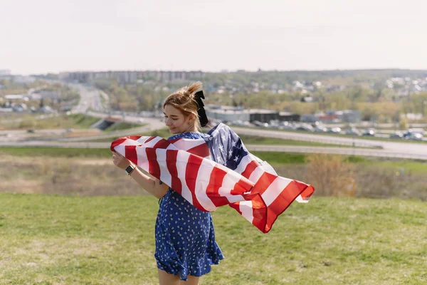Молодая женщина с национальным флагом США на плечах на фоне города празднует День независимости США — стоковое фото