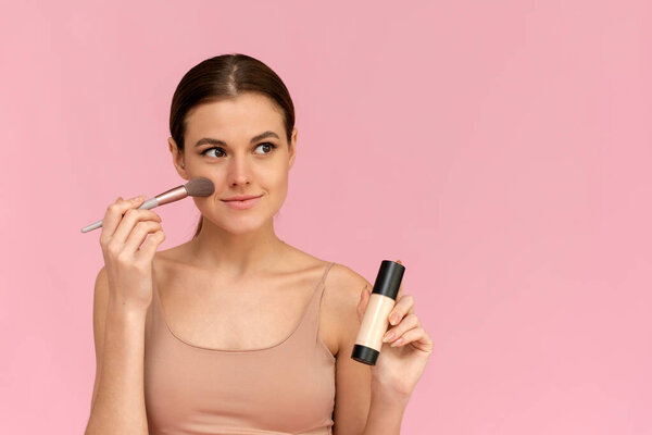 Young woman with liquid foundation. Photo of woman with perfect makeup on pink background. Beauty concept