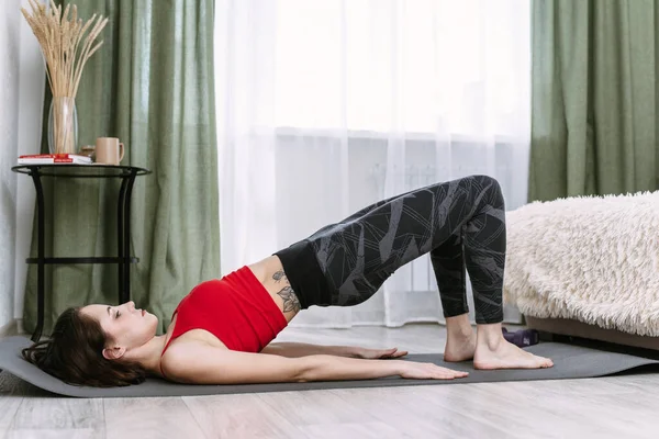 Yoga och sport hemma. En ung kvinna utför en axelbro — Stockfoto