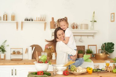 Mutlu aile sağlıklı yaşam konsepti. Annem mutfakta yemek yaparken kızına sarılıyor.