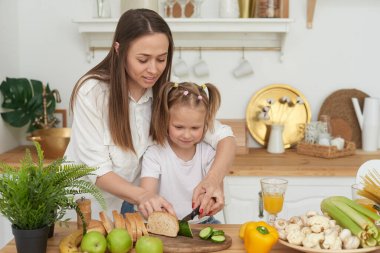 Anne, kızlarını sebze keserken kontrol ediyor. Aşçılık eğitimi