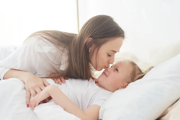 Egy boldog napra ébredni. Anya felébreszti a kislányát egy csókkal az ágyon a hálószobában. — Stock Fotó