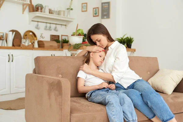 A young mother supports her daughter, calms her down and strokes her head. Little girl crying and complaining to her mother on the couch at home