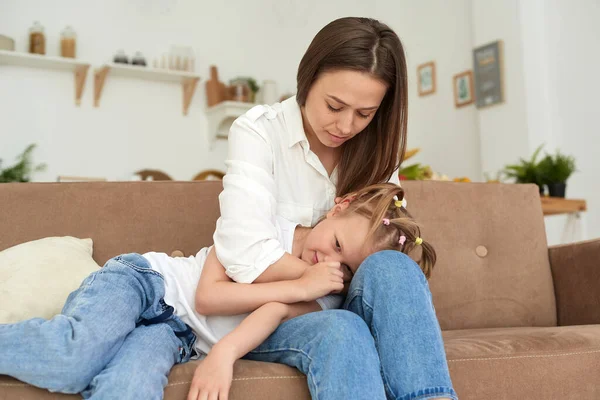 A young mother supports her daughter, calms her down and strokes her head. Little girl crying and complaining to her mother on the couch at home — Stock Photo, Image