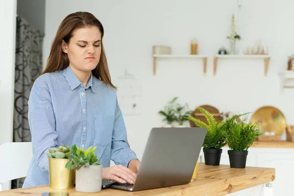 Uma mulher descontente trabalha com um laptop em casa e fica chateado com uma má conexão com a conexão à Internet, retarda o computador — Fotografia de Stock