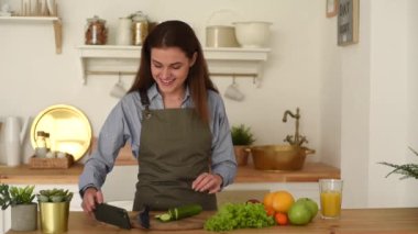 Güzel bir kadın, ahşap bir mutfakta sebze hazırlıyor ve akıllı telefondan yemek tarifine bakıyor. Genç bir kadın yemek kursu için web sitesine bakıyor ve gülümsüyor