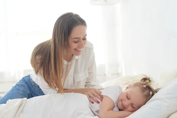 Beautiful young mom wakes up her preteen little daughter in the morning. Tenderness and care. Mothers love — Stock Photo, Image