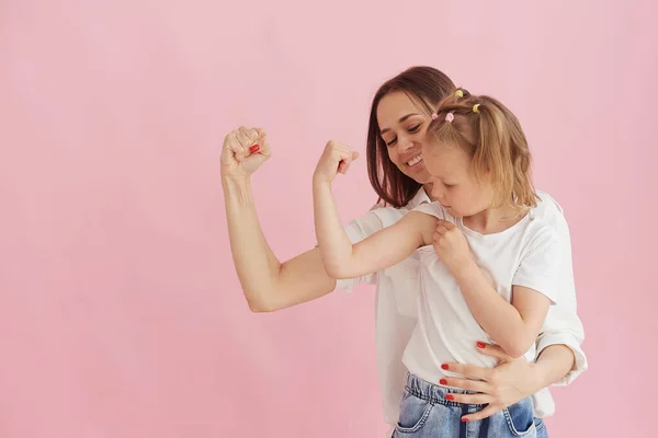 Funny family on the background of a bright pink wall. Mother and her daughter little girl having fun, showing that the strength of the muscles. Feminine power, feminism — Stock Photo, Image
