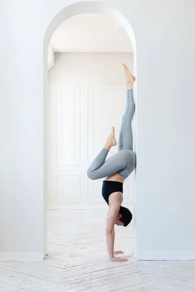 Beautiful young fitness blogger doing a difficult handstand in the light room. Concept of regular training and willpower — Stock Photo, Image