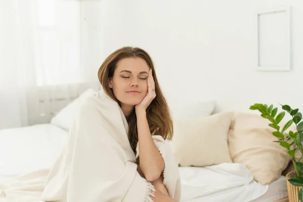 Problemas de sono, insónia. Jovem cansada em um cobertor com os olhos fechados dorme enquanto se senta na cama. É difícil para uma mulher acordar e sair da cama. — Fotografia de Stock