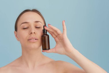 Güzel genç bir kadın cildini serumla nemlendiriyor. Cilde iyi gelir. Yaşlanma Karşıtı Terapi İçin Temel Yağ