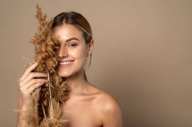 Elinde kuru otlar tutan mutlu, gülümseyen genç bir model. Buğday tanelerinden doğal kozmetik ürünleri kavramı. Cilt bakımı