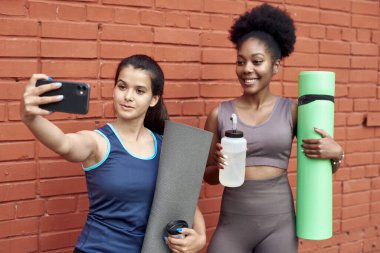 İnanılmaz genç atletik kadınların bir duvara selfie çekerken görüntüsü. Gülümseyen siyah kadınlar spor antrenmanından sonra birlikte vakit geçirirler.